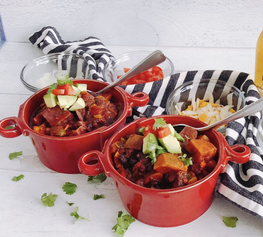 Vegetarian Sweet Potato Chili in red bowls with spoons, topped with avocado.