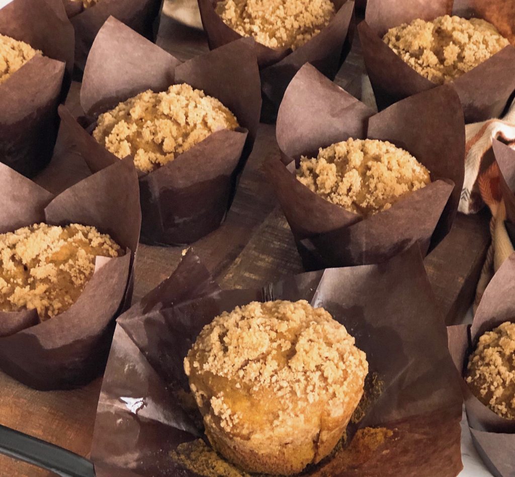 Close up of Pumpkin Streusel Muffins with brown paper muffin liner pulled down on a wooden board