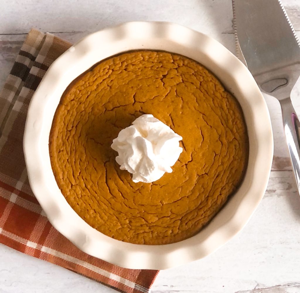 Crustless Pumpkin Pie in a white pie plate sitting on a plaid napkin.