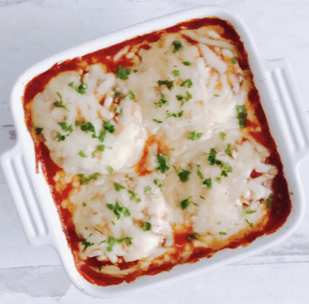 Eggplant Parmesan topped with melted mozzarella cheese in a square white baking dish