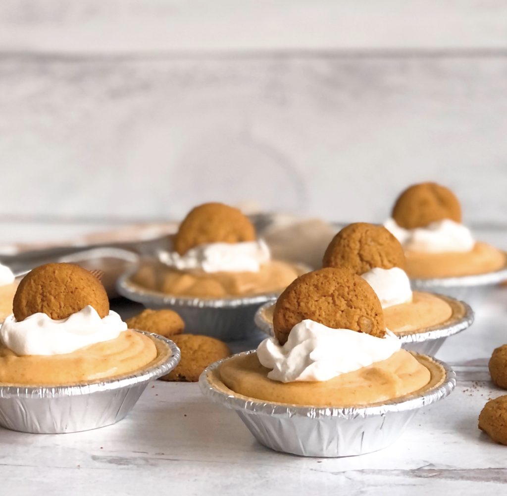 Side view of Mini Pumpkin Mousse Pies topped with gingersnaps and surrounded by gingersnaps on the table.