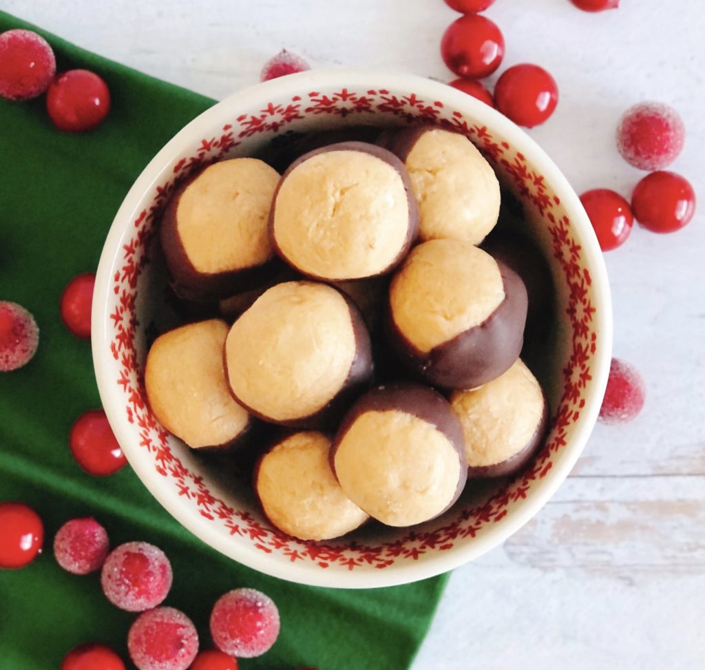 Buckeyes in a bowl on a green napkin surrounded by sugared cranberries.