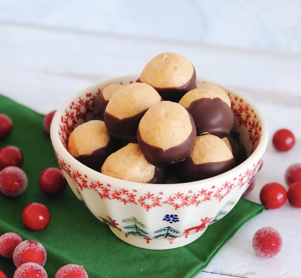 Buckeyes in a bowl on a green napkin surrounded by sugared cranberries.