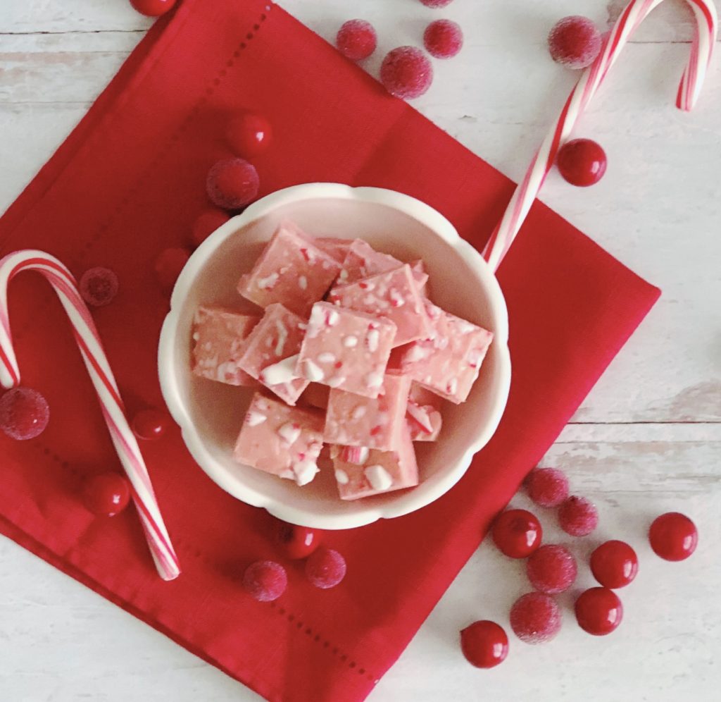 White Chocolate Peppermint Fudge in a white bowl sitting on a red napkin surrounded by sugared cranberries.