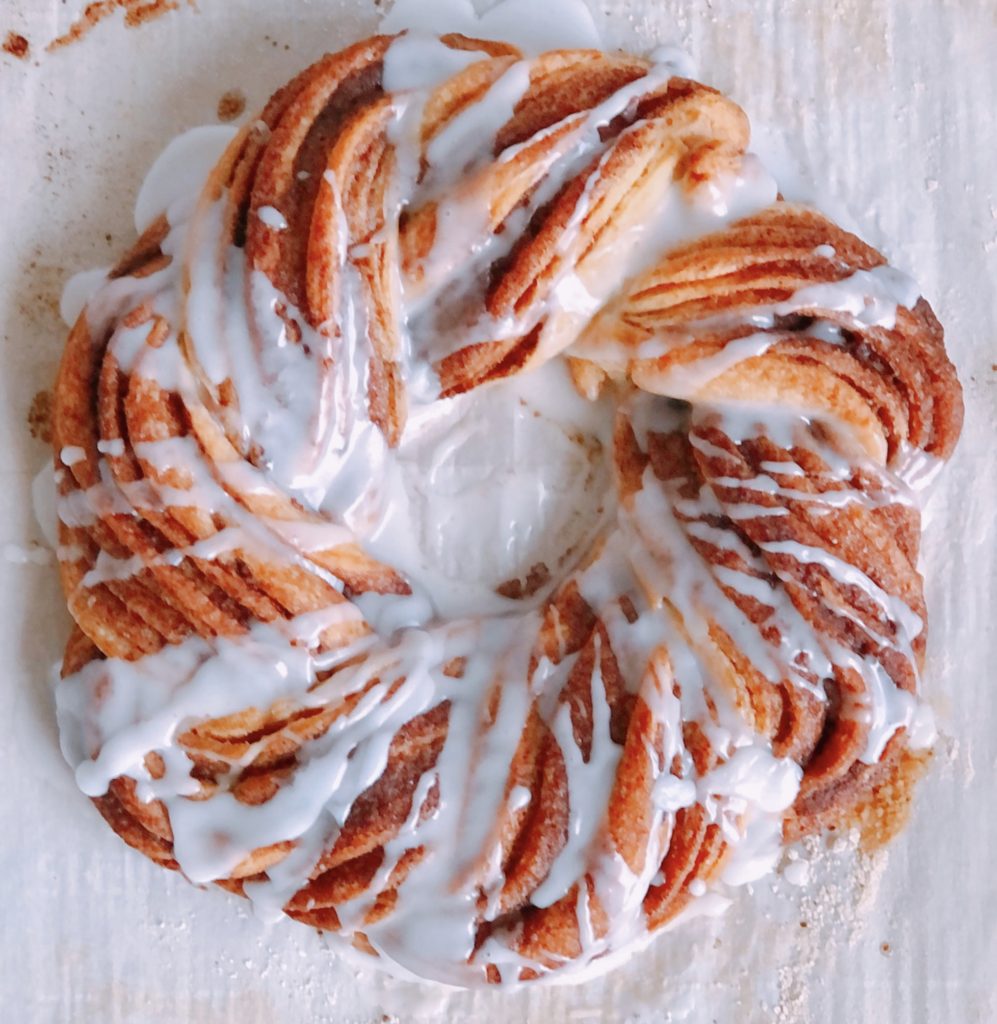 Cinnamon Roll Crescent Wreath with icing drizzled over top on parchment paper.
