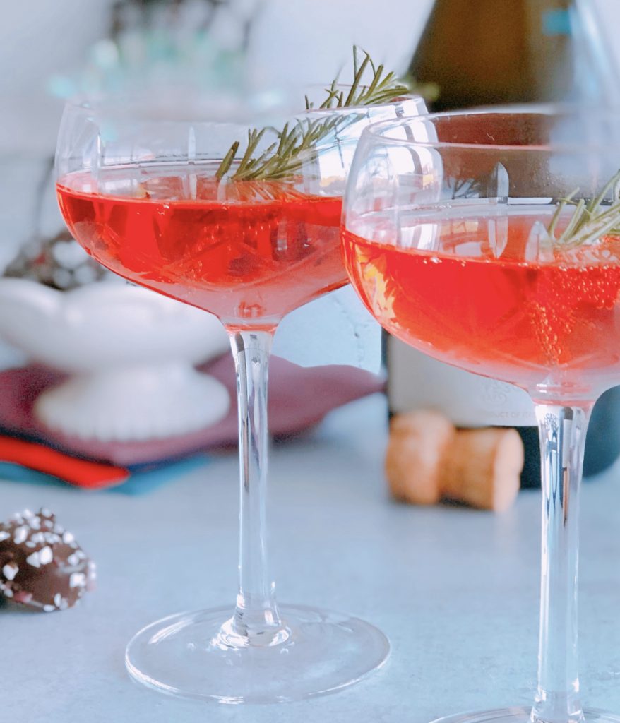 Holiday Mimosas in a coupe glass with sprig of rosemary.
