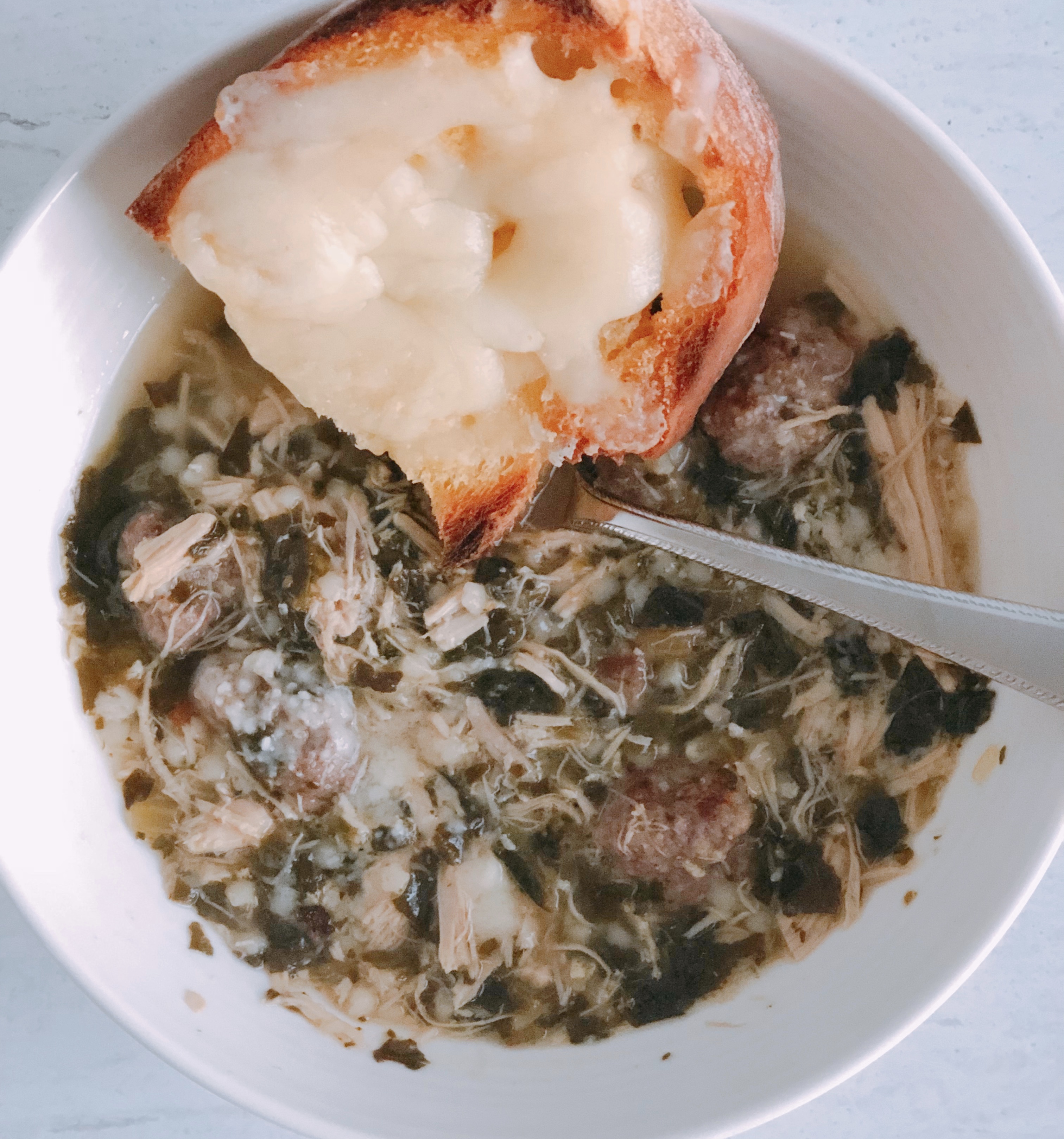 Italian Wedding Soup in a bowl with a spoon and a piece of cheese toast.