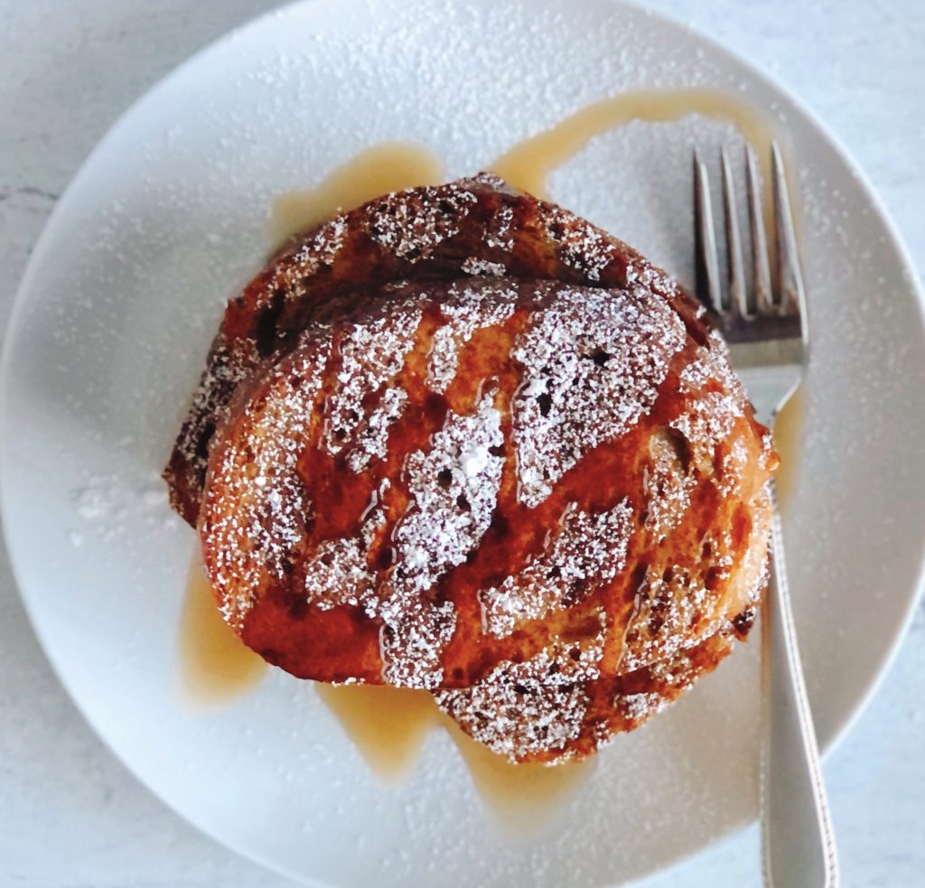 Sheet Pan French Toast stacked on a plate topped with maple syrup.