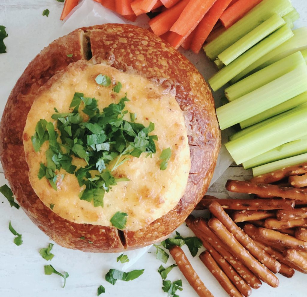 Parmesan Bread Bowl Dip topped with parsley surrounded by carrots, celery and pretzels.