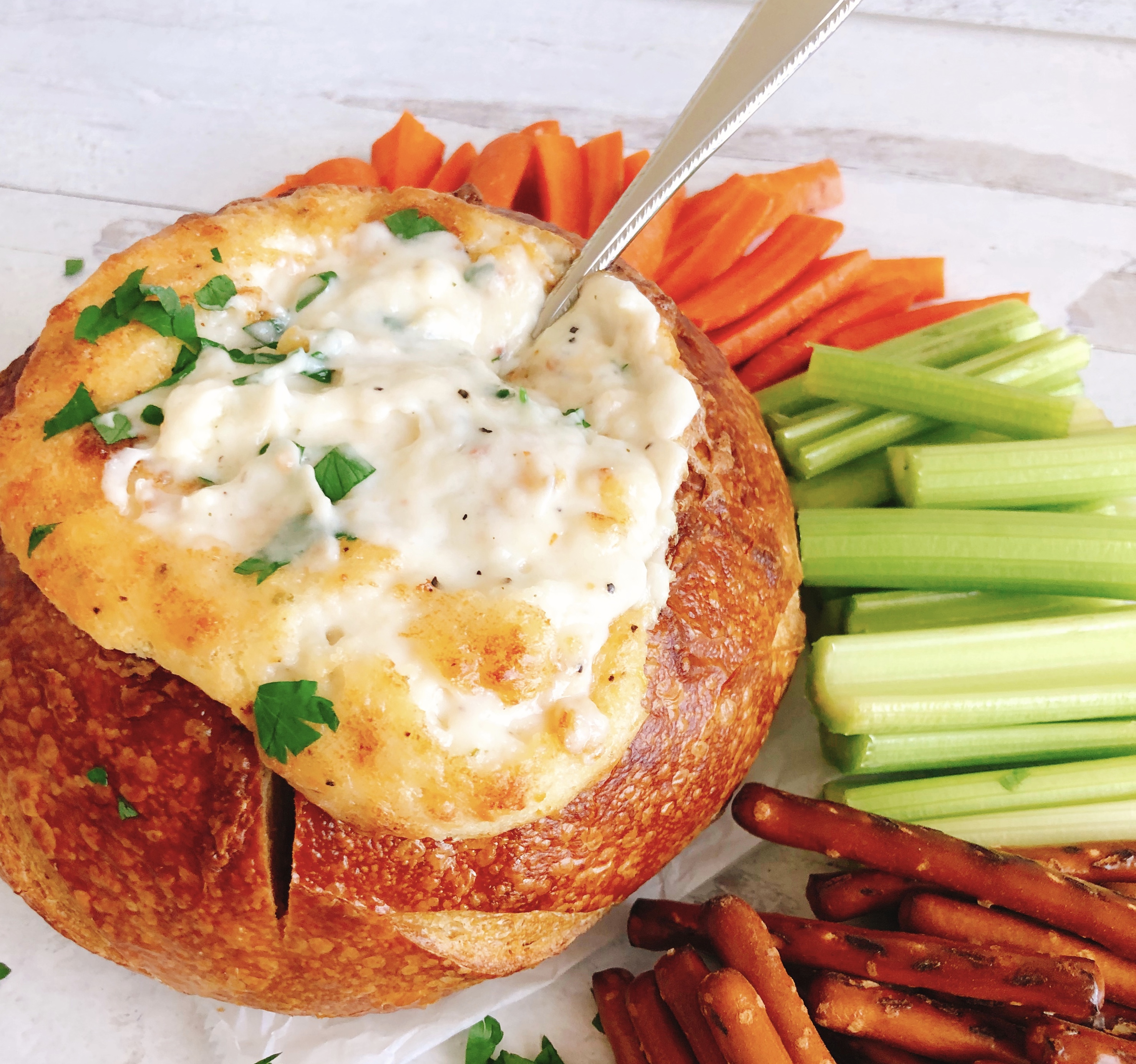 Parmesan Bread Bowl Dip with a spoon surrounded by carrots, celery and pretzels.