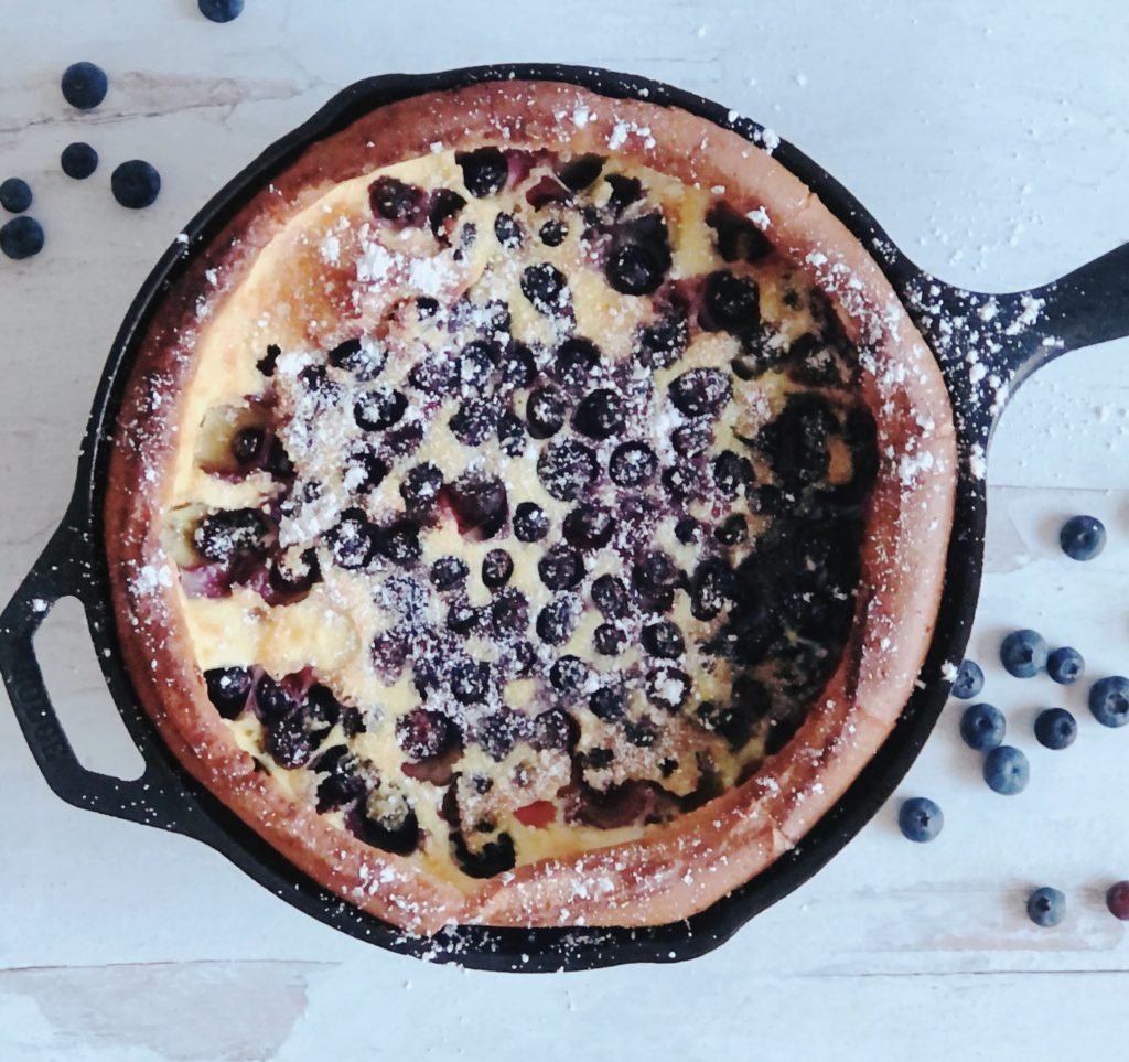 Blueberry Dutch Baby in a cast iron skillet sprinkled with powdered sugar.