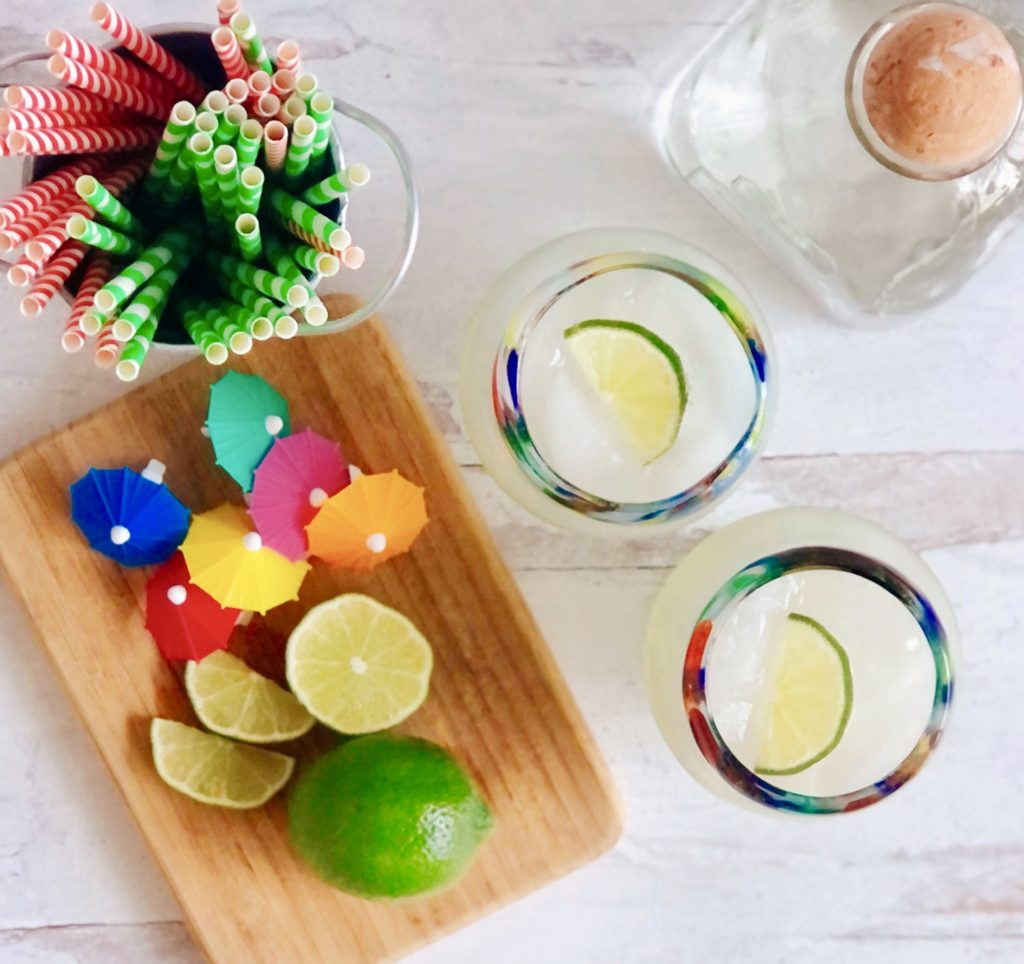 Skinny Ginger Lime Margarita with slice of lime, next to cutting board with lime and little umbrellas