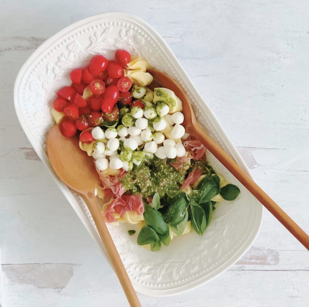 Caprese Pesto Tortellini Salad in a white oval bowl with wooden serving spoons