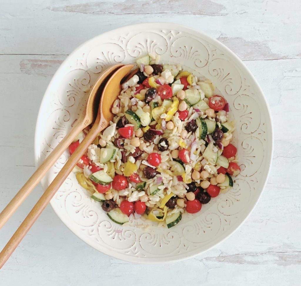 Greek Orzo Salad in a white bowl with wooden salad spoons