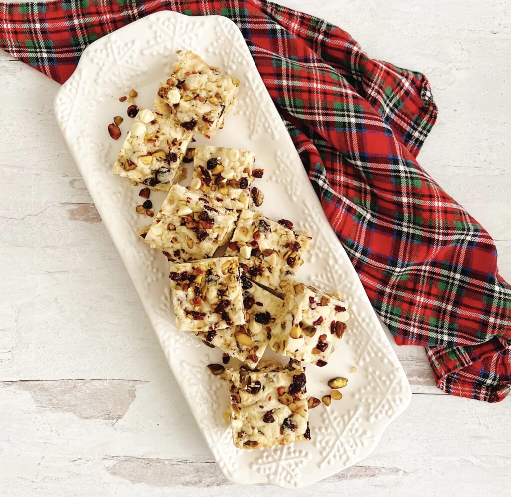 White Chocolate Cranberry and Pistachio Bars on a white platter with a Christmas plaid napkin